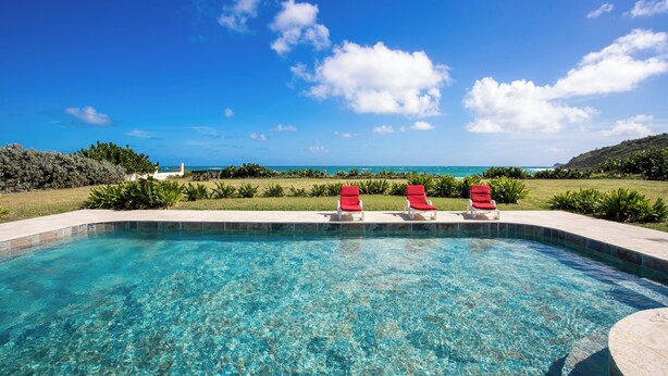 A clear blue pool with three red lounge chairs and a view of the ocean. - Direct Beachfront 6 BDR/en-suite /maid included. Excellent service. Rare gem (A) (Guana Bay Beach)