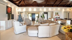 A spacious living room with a high ceiling, a white sofa set, a small Christmas tree, and a ceiling fan. - Direct Beachfront 6 BDR/en-suite /maid included. Excellent service. Rare gem (A) (Guana Bay Beach)