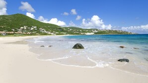 A beach with clear turquoise water, white sand, and a small village on a green hill in the background. - Direct Beachfront 6 BDR/en-suite /maid included. Excellent service. Rare gem (A) (Guana Bay Beach)