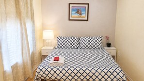 A hotel room with a bed, a nightstand, a lamp, a framed picture on the wall, and a window with curtains.