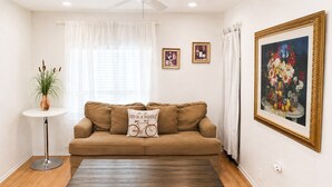 A living room with a brown sofa, a round coffee table, a potted plant, and a framed painting on the wall. - Walkable Roosevelt Row / 1BR 1BA Downtown Stay (Phoenix)