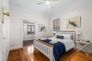 A bedroom with a white bed, a wooden headboard, a nightstand, and a ceiling fan.