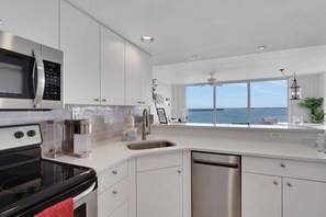 A modern kitchen with a view of the sea, stainless steel appliances, and white cabinetry. - Romantic 5th-Floor Bayfront Retreat | Dolphins, Sunrise Views, Heated Pool, Hot Tub, Beach Gear! (Fort Myers Beach)
