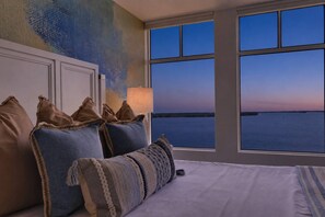 A bedroom with a large window, a bed, and a wall with a textured mural. - ROMANTIC 5TH-FLOOR BAYFRONT RETREAT | DOLPHINS, SUNRISE VIEWS, POOL, HOT TUB, BEACH GEAR! (Fort Myers Beach)