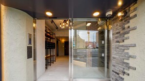 A modern entrance with glass doors, a staircase, and a brick wall. - RESI STAY BRiX (Kyoto)