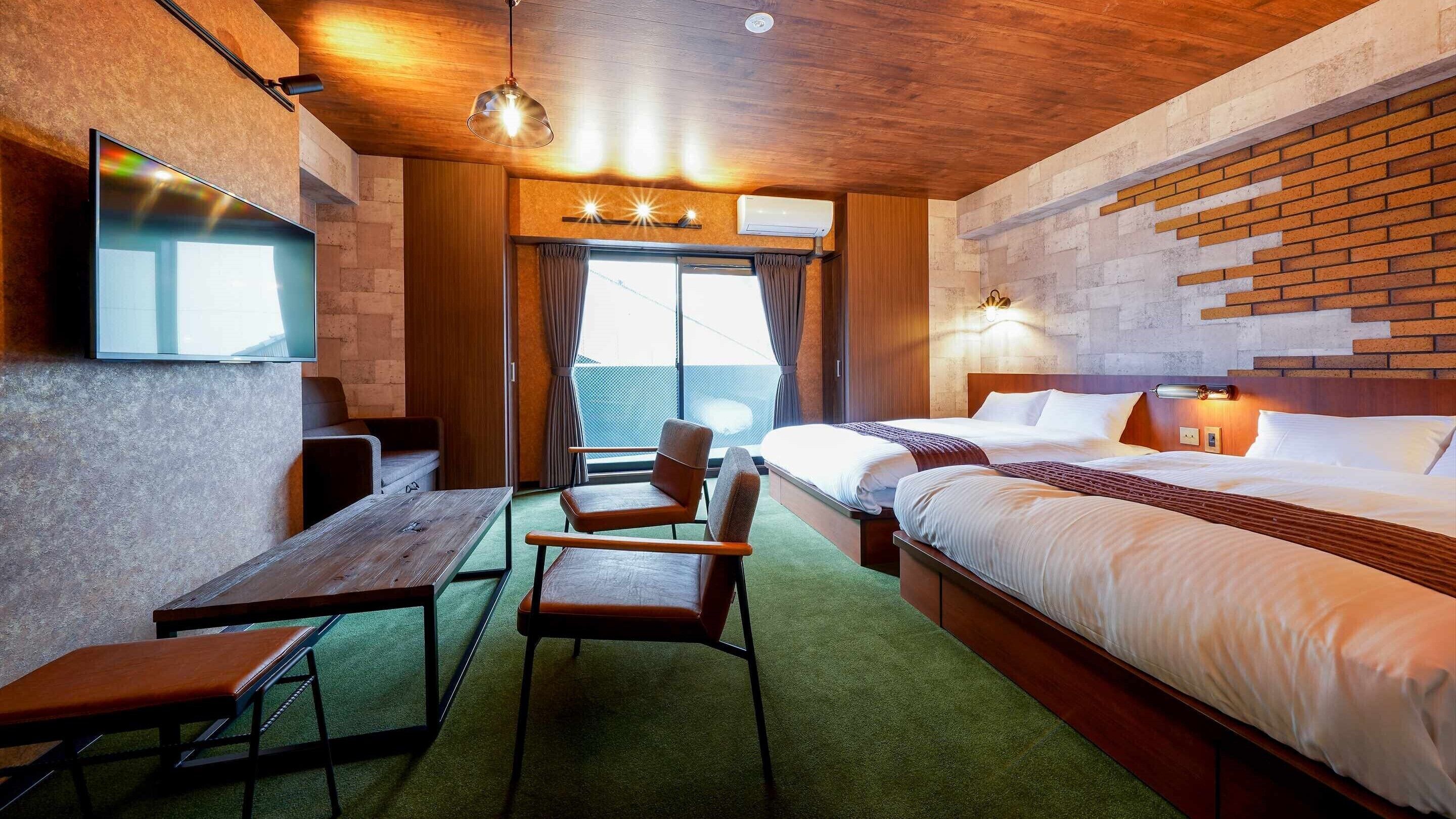 A hotel room with a bed, a desk, chairs, a TV, and a window with curtains.