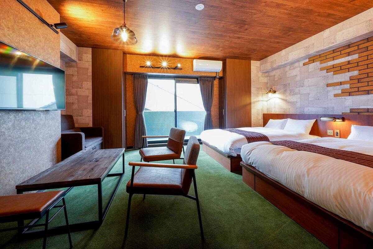 A hotel room with a bed, a desk, chairs, a TV, and a window with curtains.