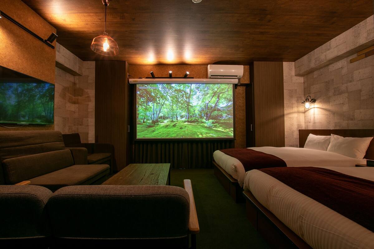A cozy room with a large screen displaying a forest scene, a bed, a sofa, and a wooden table.
