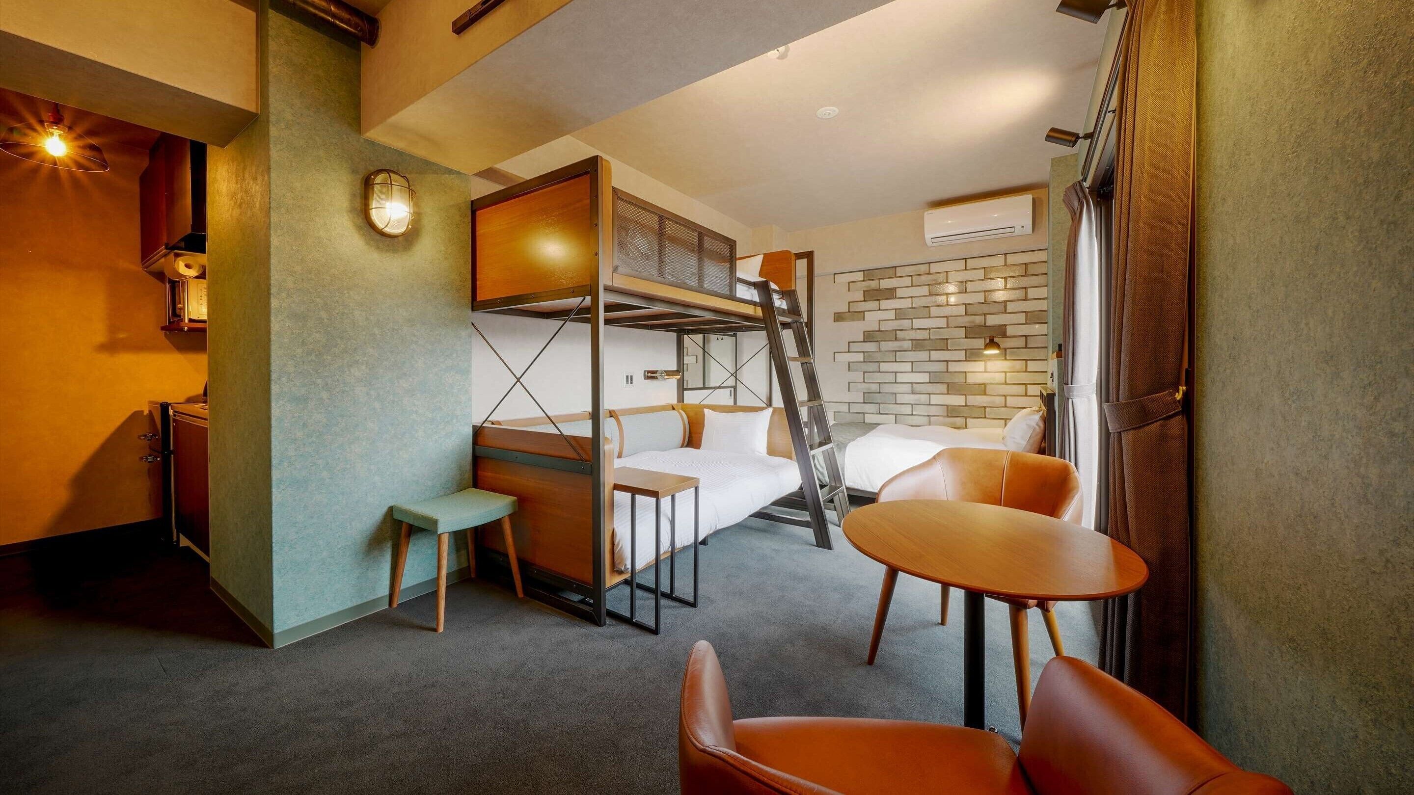 A compact hotel room with a bunk bed, a small table, a chair, and a sofa.