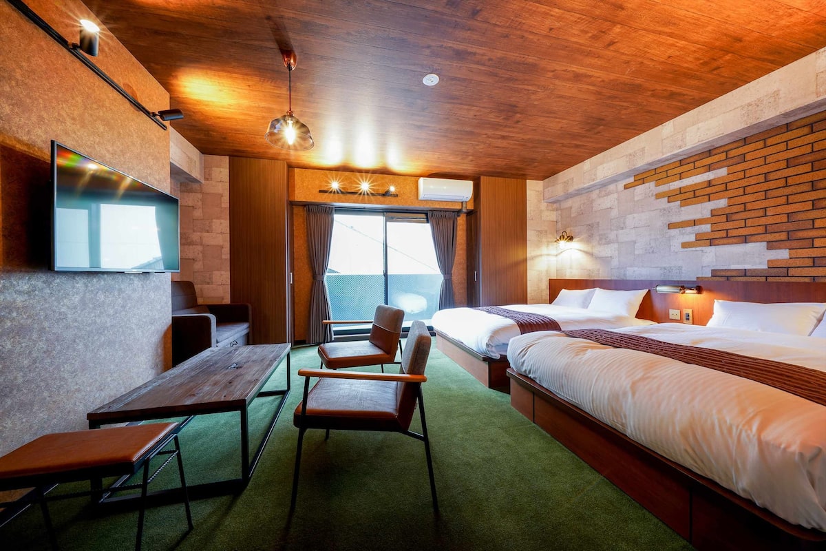 A modern hotel room with a wooden ceiling, a large bed, a desk with a chair, a TV, and a window with curtains.