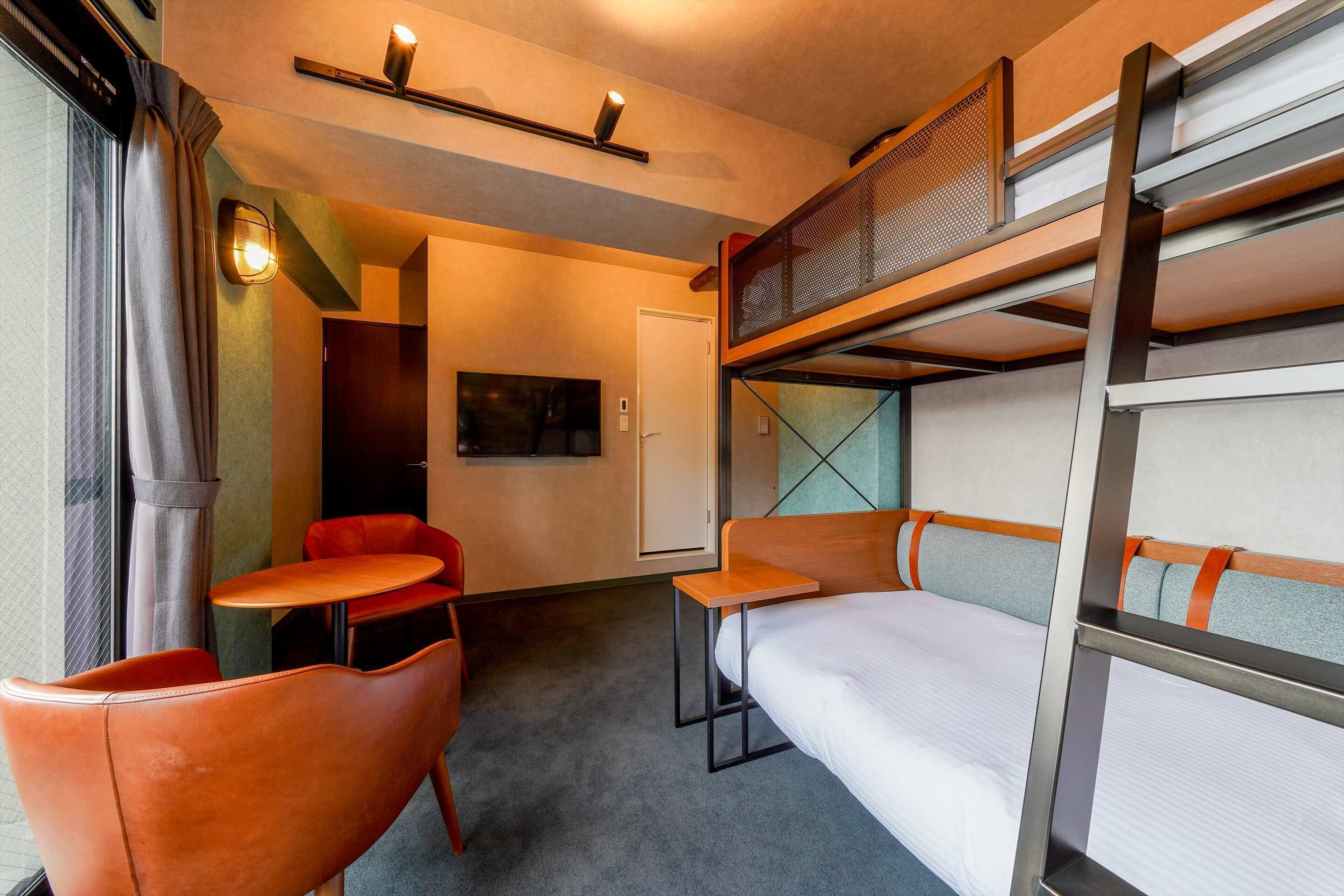 A compact hotel room with bunk beds, a small table, and two chairs.
