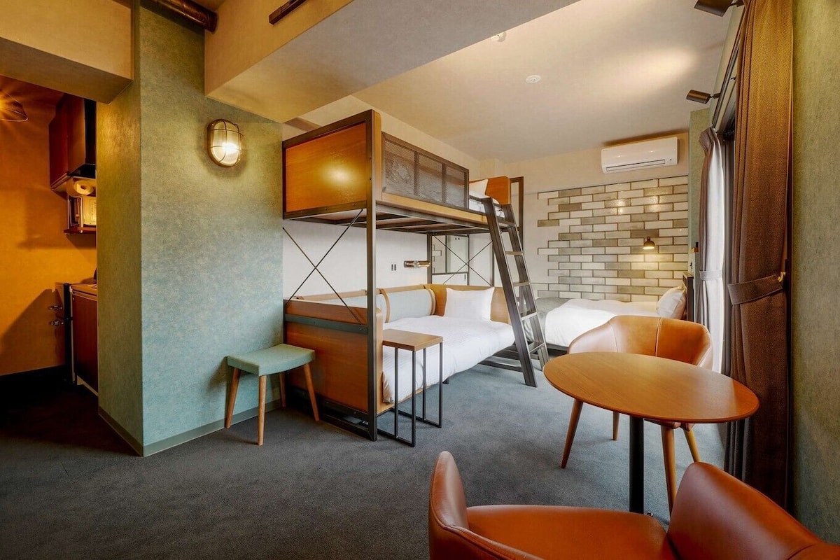 A compact room with a bunk bed, a small table, a chair, a desk, and a ladder.