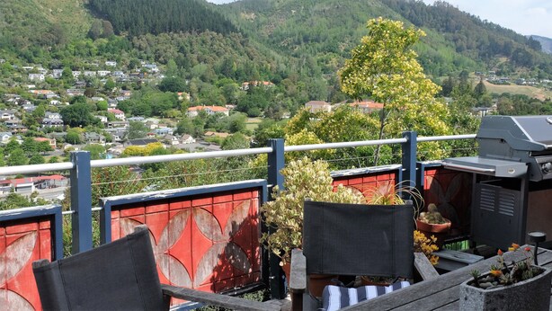 A balcony with a view of a residential area, a barbecue grill, and potted plants.