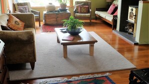 A spacious living room with a large window, a wooden coffee table, a colorful rug, and a fireplace.