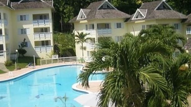 Ett semesterområde med en swimmingpool, flervåningsbyggnader och frodig grönska.