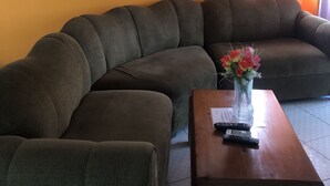 Ett vardagsrum med en hörnsoffa, ett soffbord i trä och en vas med blommor.