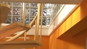 En tv-apparat står på ett träställ i ett rum med orange väggar och en trappa.