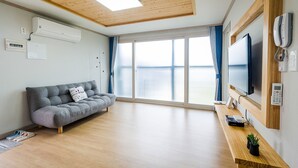 Una sala de estar moderna con un sofá gris, piso de madera, un televisor grande y techo de madera.