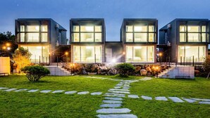 Una casa moderna de varios pisos con grandes ventanales, un camino de piedra que lleva a la entrada y un césped cuidado.