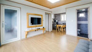 Amplia sala de estar con techo de madera, televisor montado en la pared, mesa de comedor con sillas y sofá gris.
