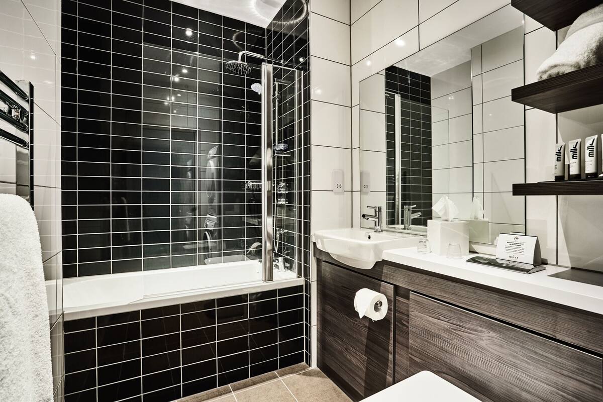A modern bathroom with a glass-enclosed shower, a large mirror, and a vanity with a sink and towel rack.