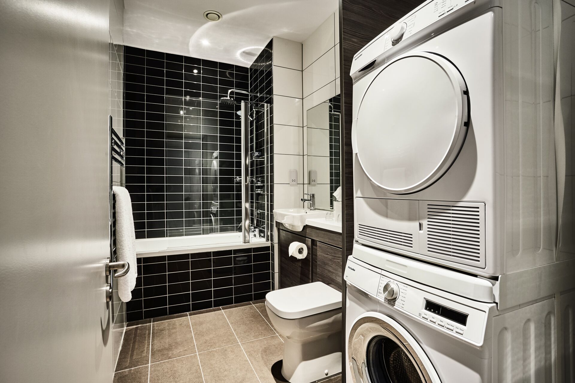 Une salle de bain moderne avec une douche aux carreaux noirs, des toilettes et un appareil combiné lave-linge et sèche-linge.