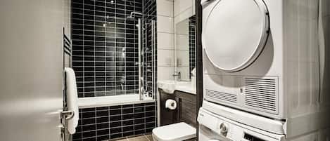 A modern bathroom with a black-tiled shower, a toilet, and a stacked washer and dryer unit.