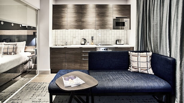 A modern hotel room with a sofa, a small table, a bed, a kitchenette, and a large window with curtains. - Citadines City Centre Liverpool (Liverpool)