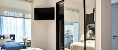 A modern hotel room with a large bed, a desk, and a TV mounted on the wall.