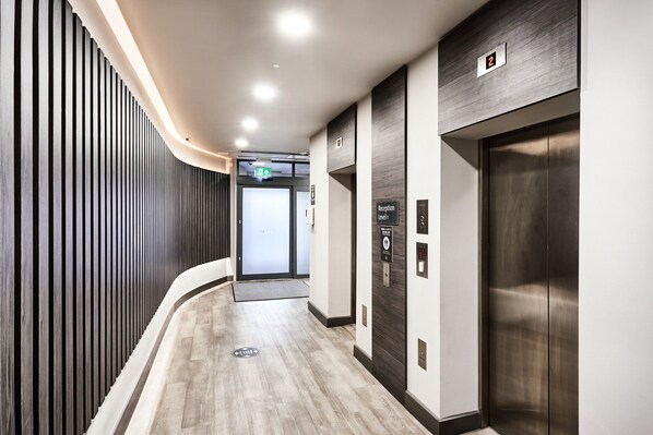 A modern hallway with a wooden slat wall, a reception desk, and an elevator. - Citadines City Centre Liverpool (Liverpool)
