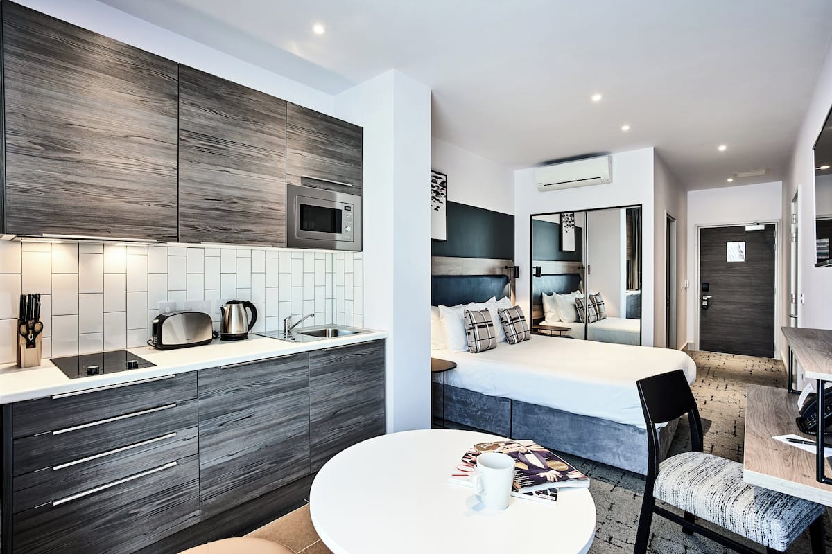 Una habitación de hotel moderna con cocina, una cama con cabecero y un comedor.