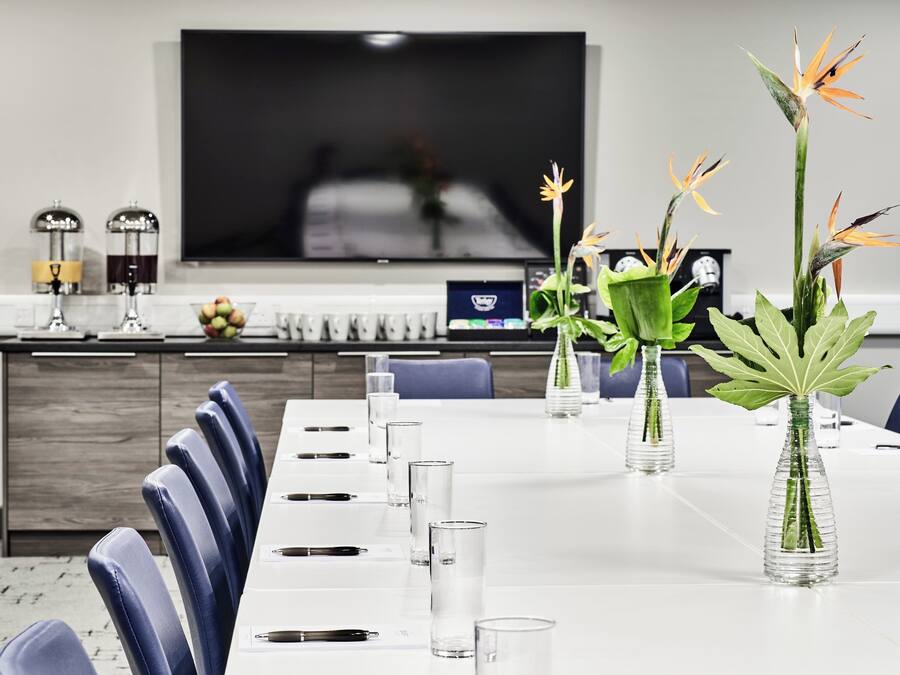 A modern dining area with a long table, chairs, and vases with flowers.