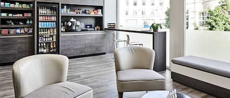 A modern hotel room with a seating area, a minibar, and a view of the city.
