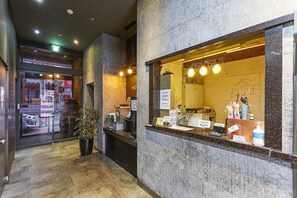 A hotel reception area with a marble counter, a potted plant, and a visible window to the outside.