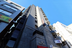 A modern hotel building with a prominent 'HOTEL HERTZ' sign, multiple balconies, and a clear sky.