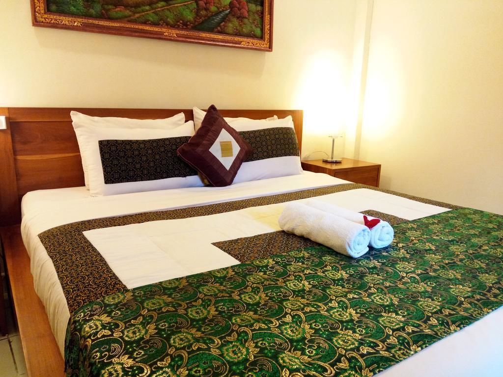 Una cama bien hecha con una colcha verde estampada, almohadas blancas y una toalla enrollada sobre la cama.