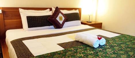 A neatly made bed with a green patterned bedspread, white pillows, and a rolled towel on the bed.