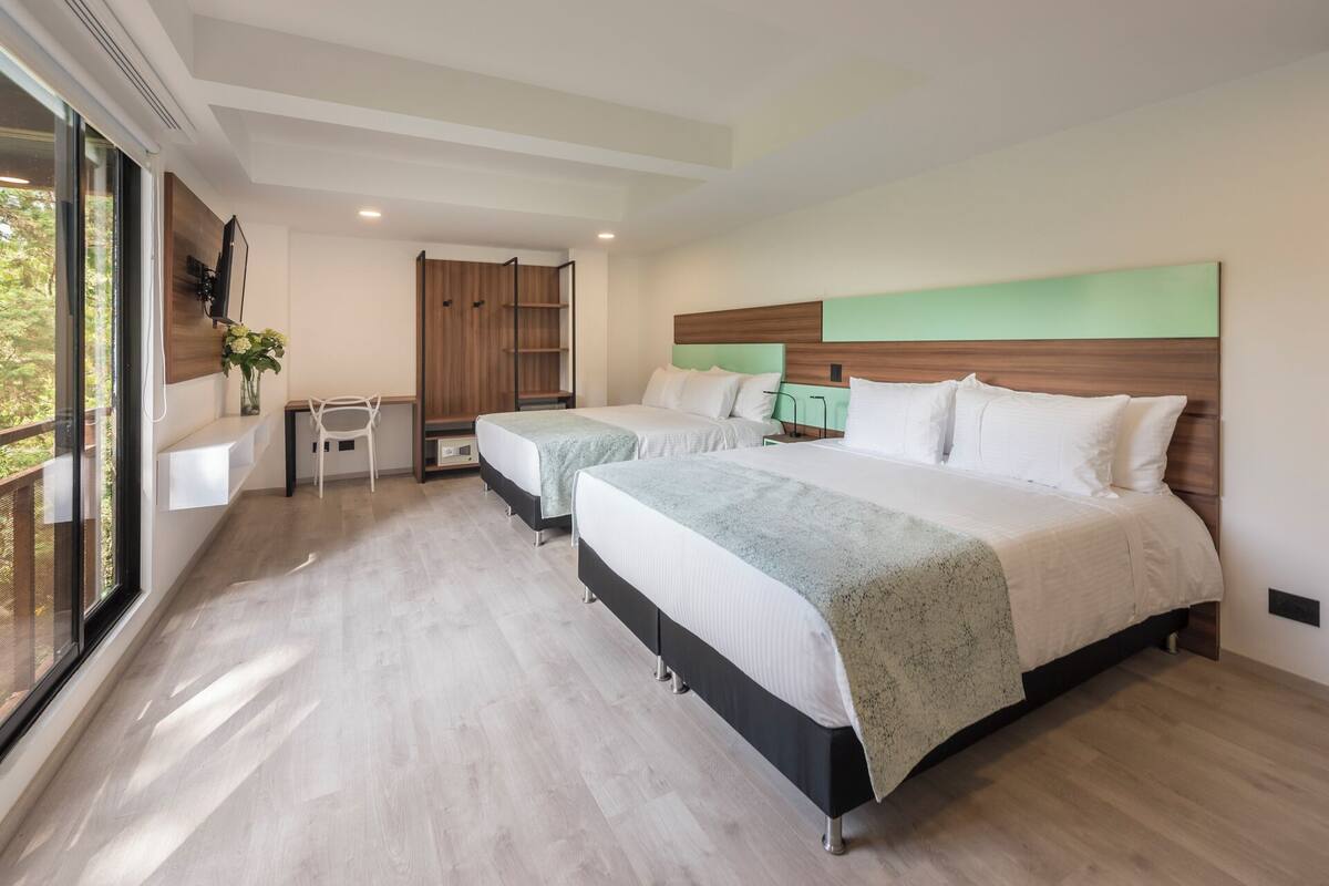 A modern hotel room with two beds, a desk, and a wardrobe.