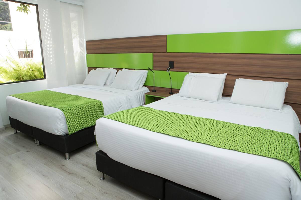 Two twin beds with green and white bedding, wooden headboards, and a window with a view of greenery.