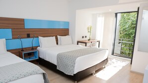 A modern hotel room with two beds, a wooden headboard, a small table with a plant, and a view of greenery through a glass door. - Foresta Hotel (Medellín)