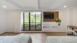 A modern room with a large sliding glass door, a mounted TV, a small white console table, and a white chair. - Foresta Hotel (Medellín)