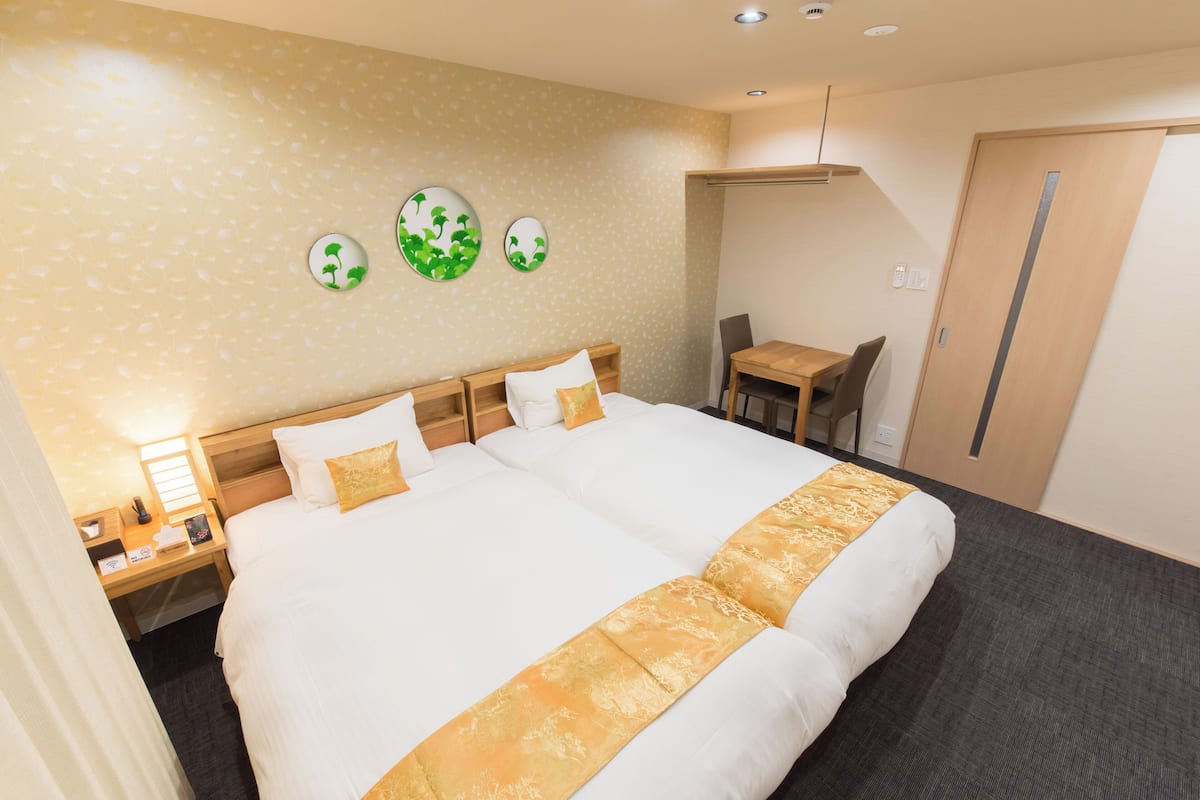 A hotel room with a large bed, a desk with a chair, a small table, and a door.