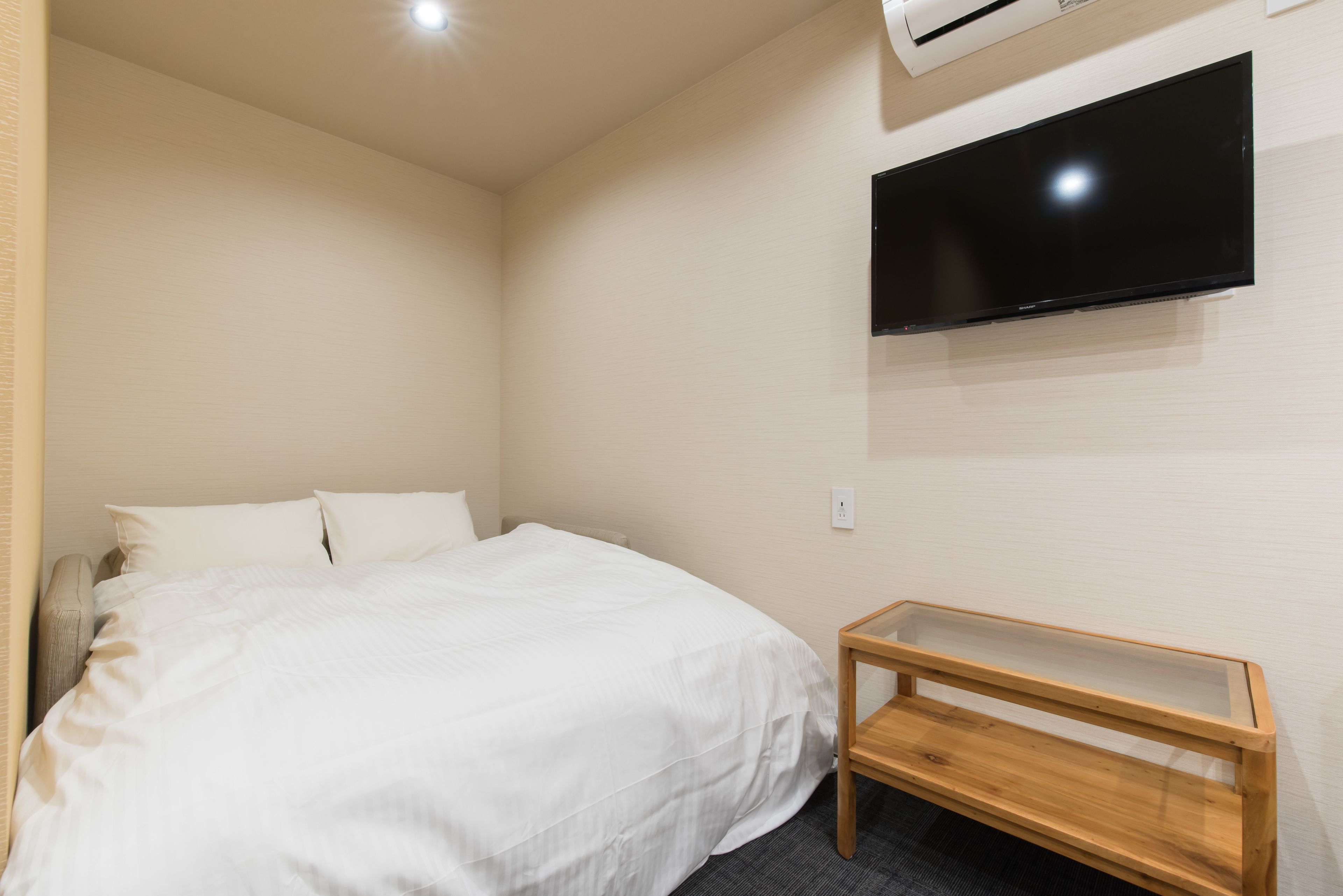 A bedroom with a bed, a TV mounted on the wall, and a small wooden bench.