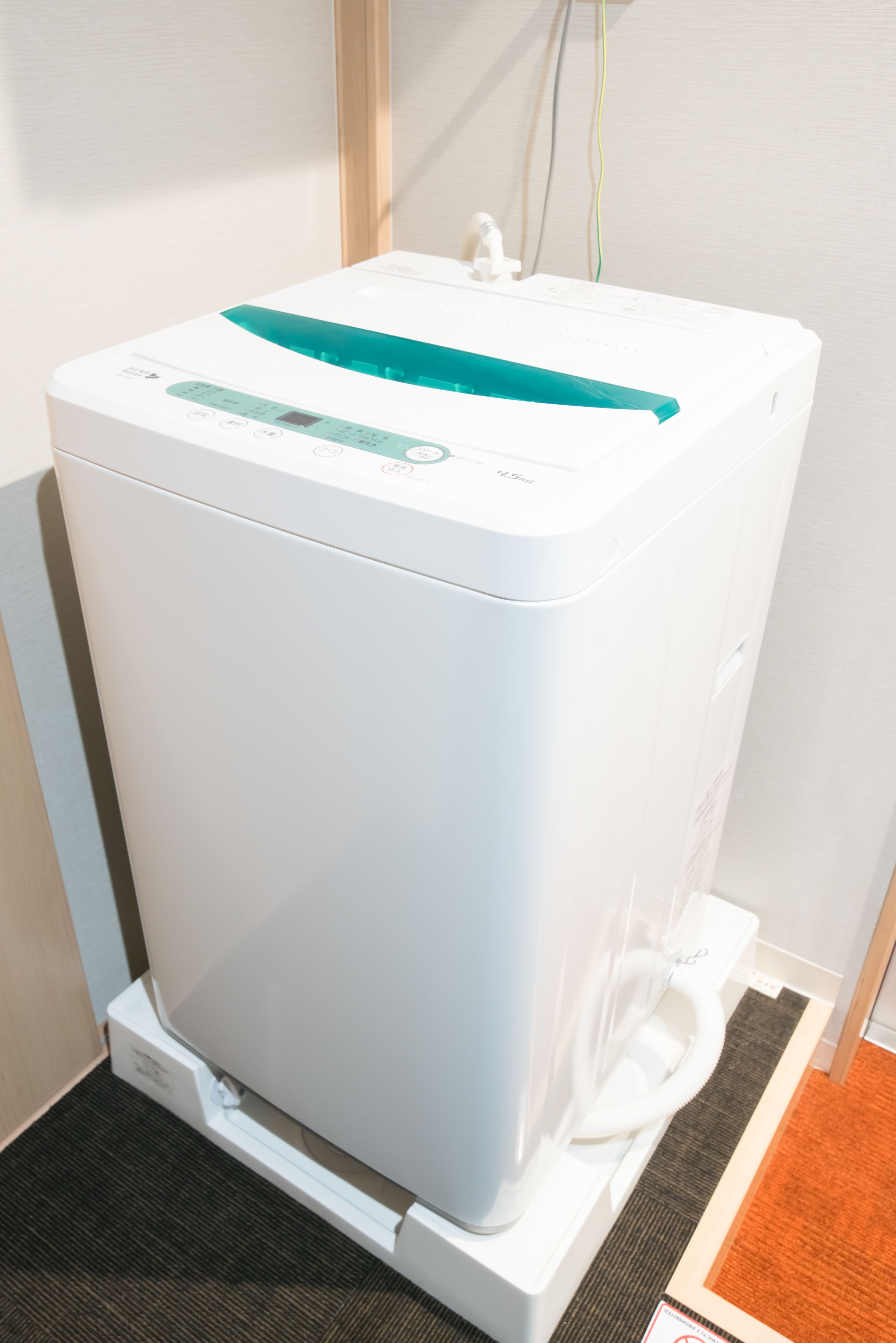 A white portable water heater with a digital display and a control panel, placed on a carpeted floor next to a wall with electrical outlets.