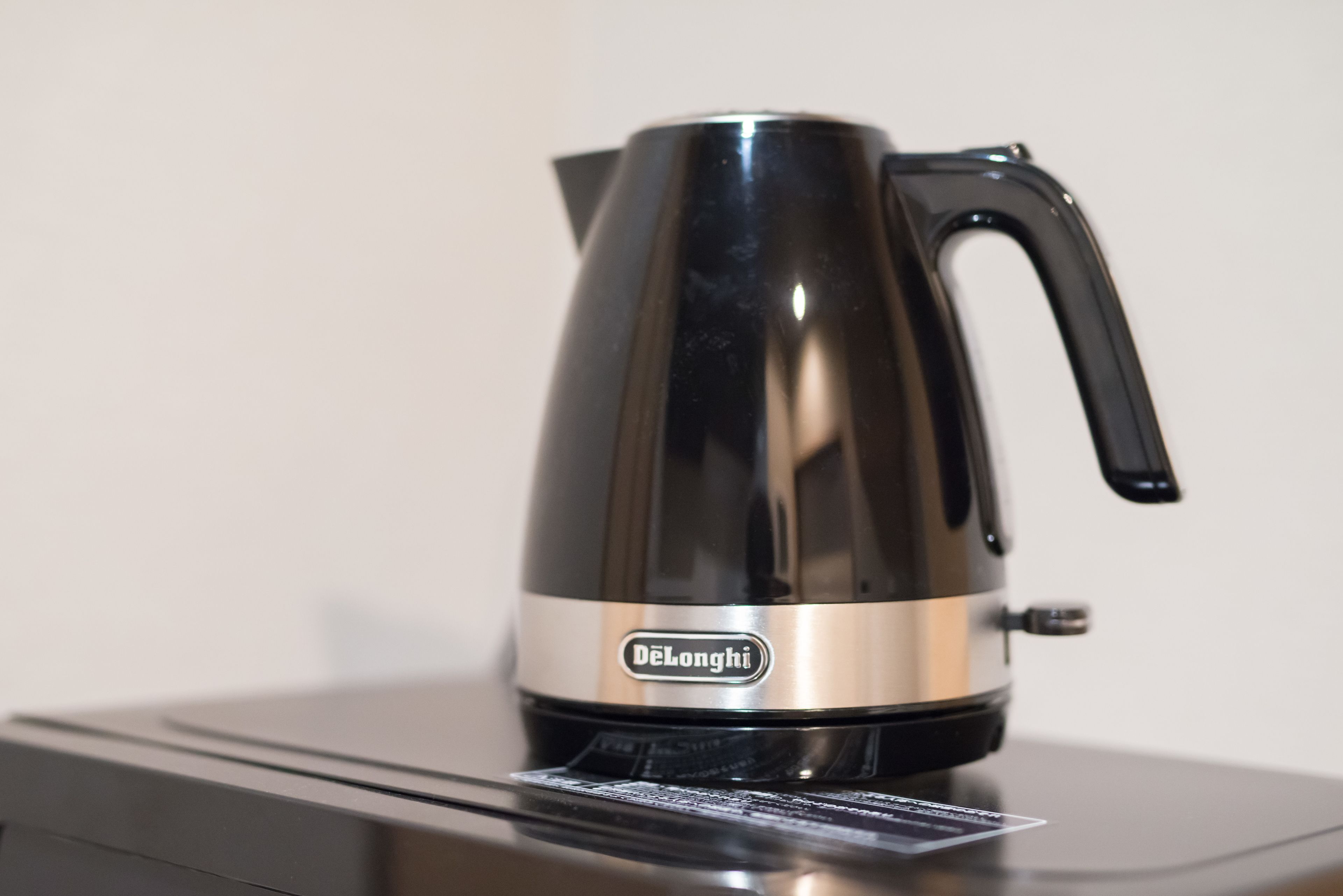 Une bouilloire électrique DeLonghi, de couleur noire et argentée, posée sur un plan de travail moderne dans une cuisine.
