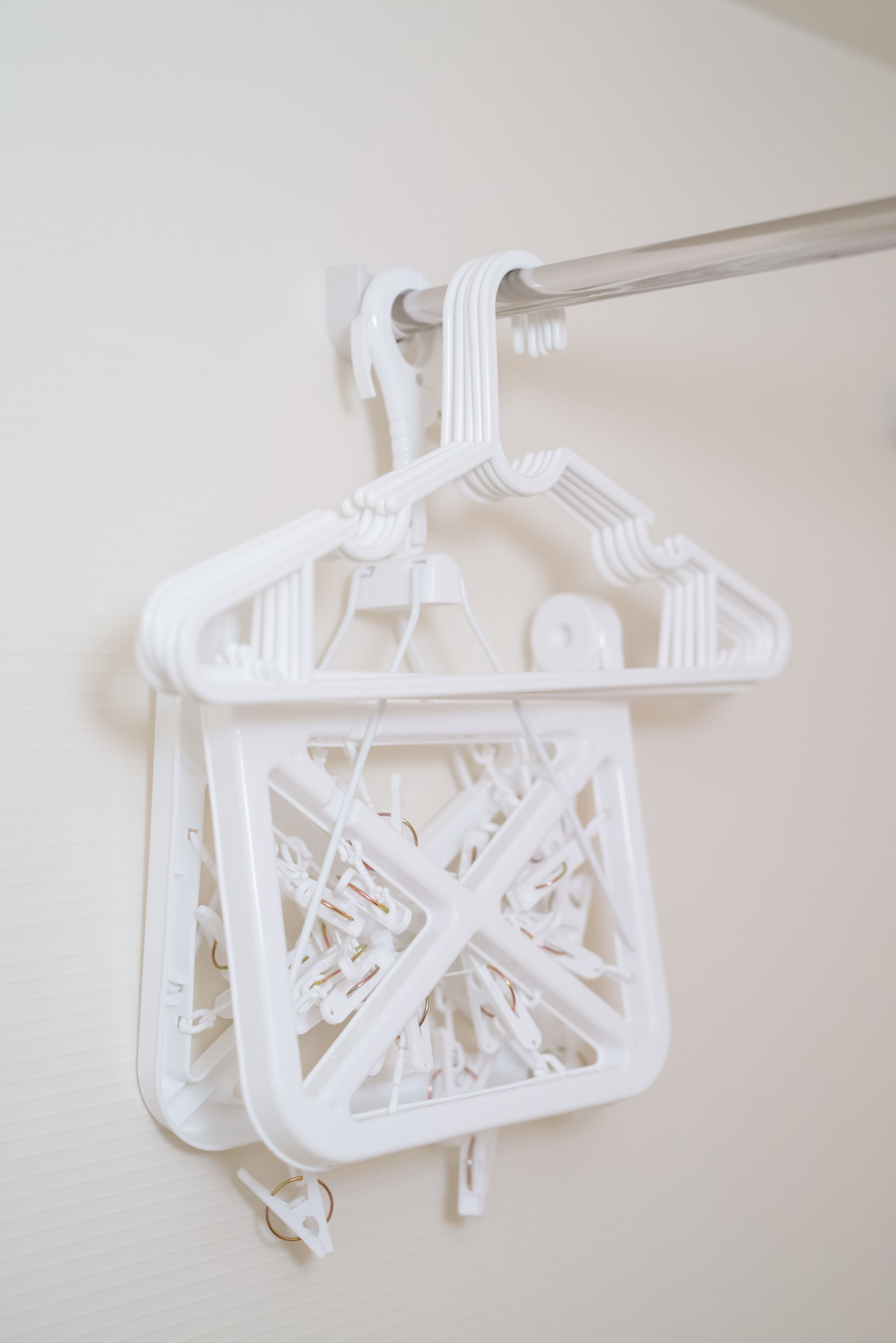 A white plastic laundry basket with a handle, hanging on a white wall.