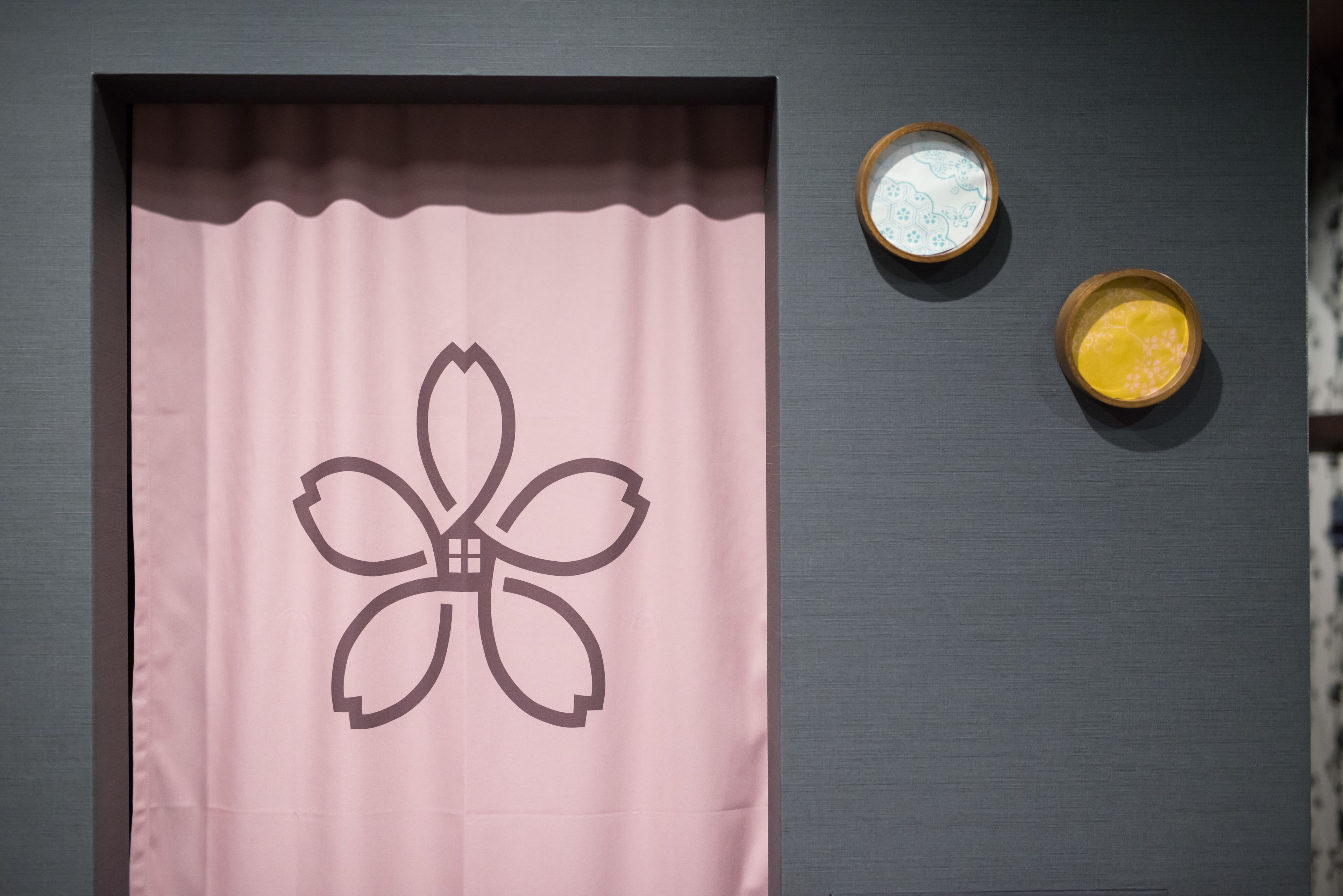 A pink curtain with a floral design, two small bowls with different contents, and a dark wall.