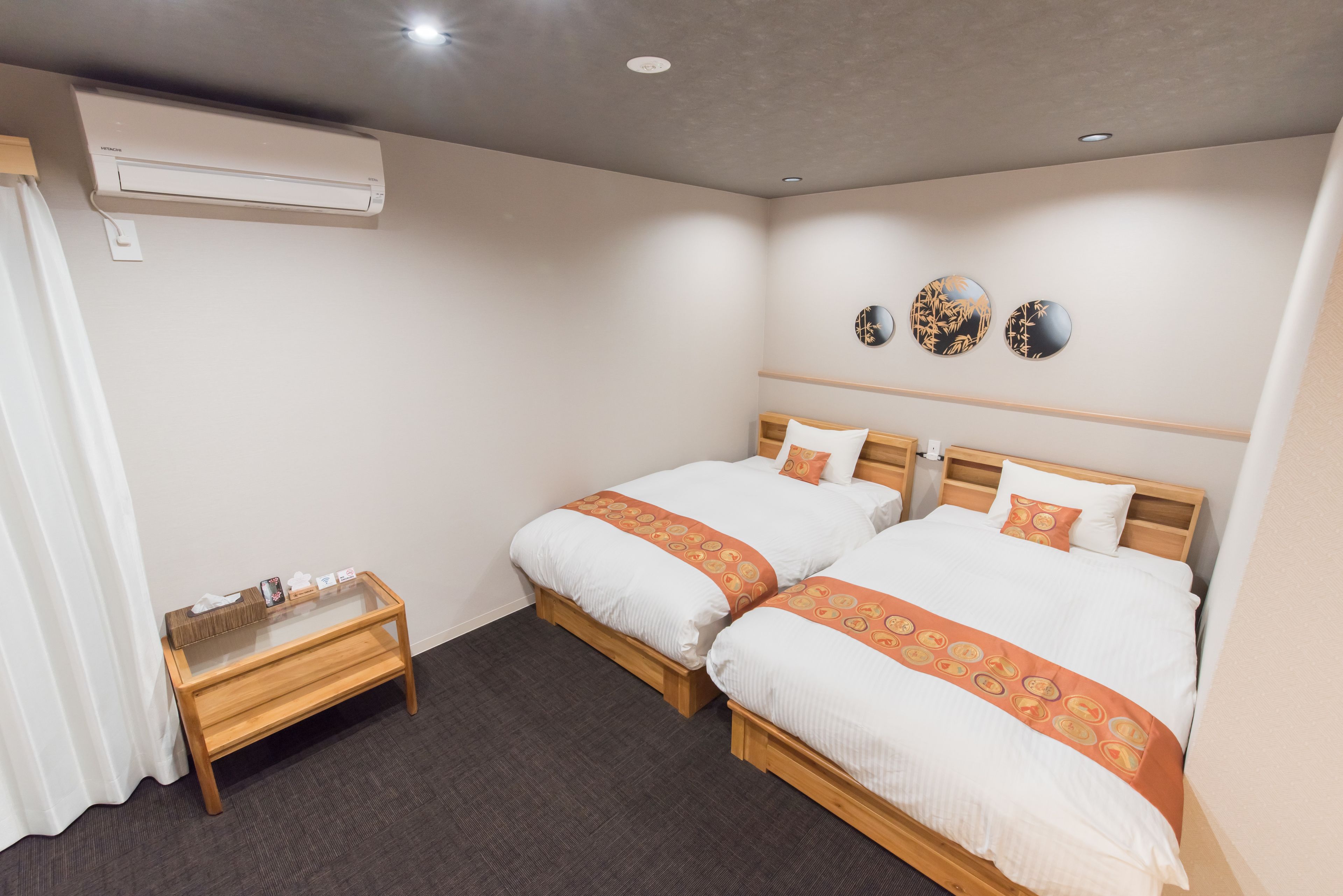 A hotel room with two beds, a small wooden table, and an air conditioning unit.