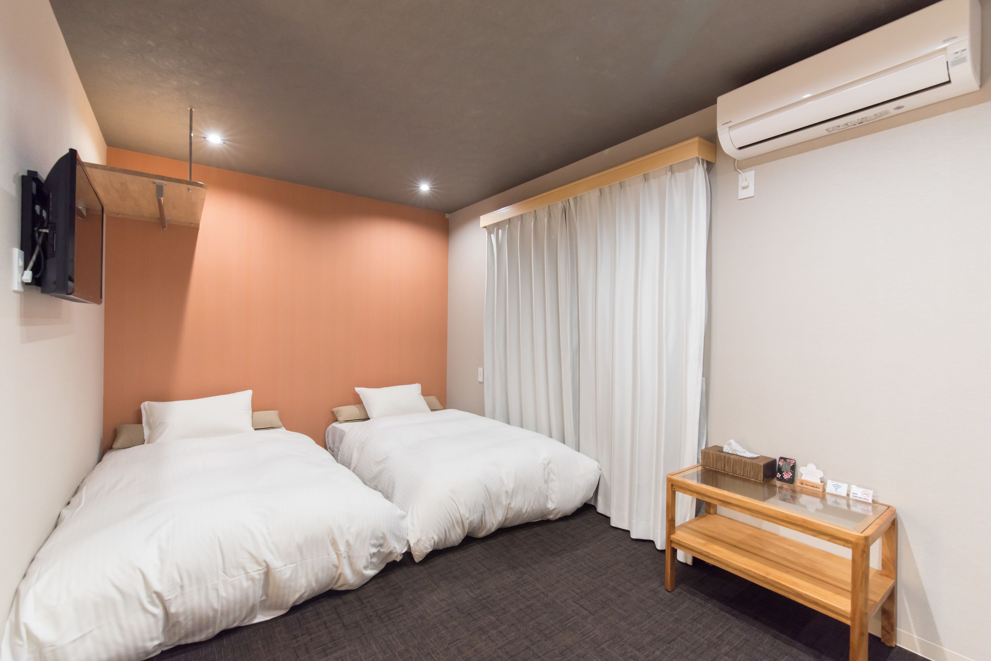 A hotel room with two single beds, a wooden nightstand, an air conditioning unit, and a mirror on the wall.