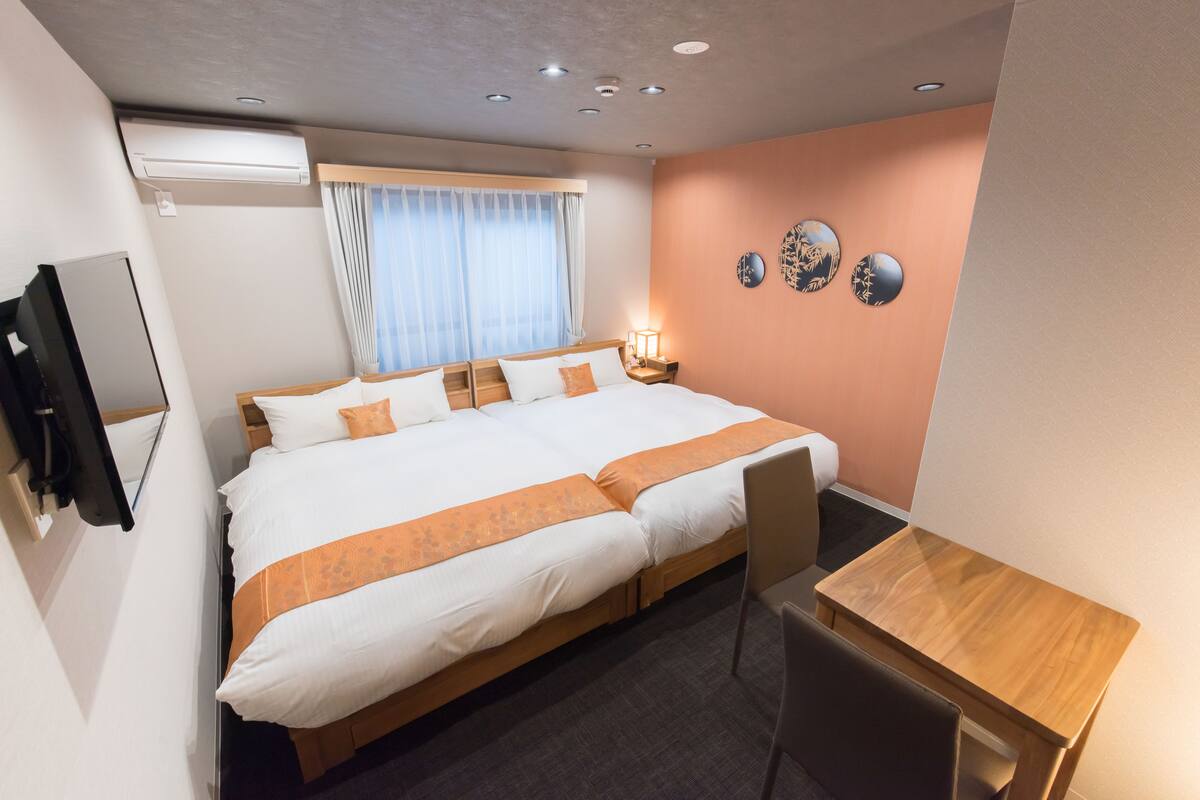 A hotel room with a large bed, a desk, a TV, and a wall-mounted air conditioner.